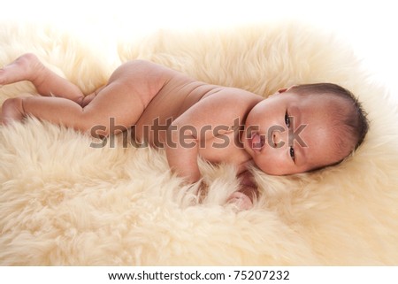 A beautiful oriental baby laying on a fur rug without her clothes on with her tongue sticking out.