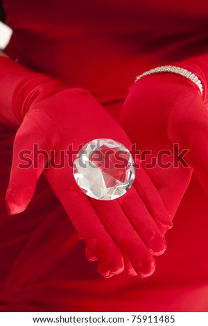 A woman in a red dress with red gloves holding onto a giant gem.