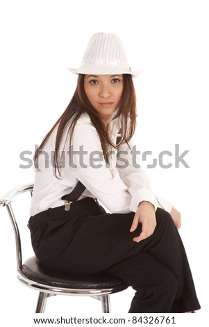 a woman in her hat and suspenders sitting on a stool with a serious expression on her face.