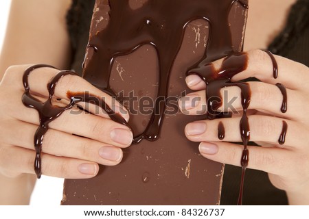 A woman\'s hands holding on to a chocolate candy bar with chocolate syrup all over her fingers.