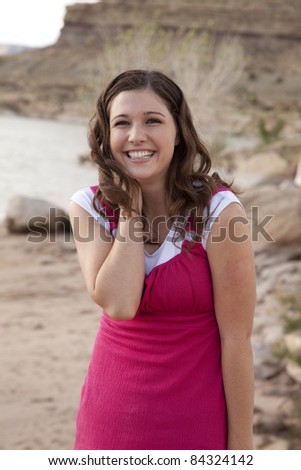 a woman with a happy expression on her face while she is in the outdoors by a lake and rocks.