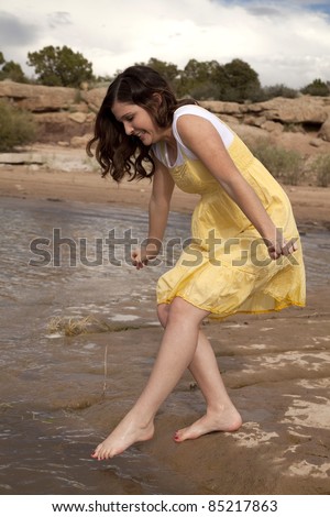 A woman tip toe into the water with a uncertain look on her face.