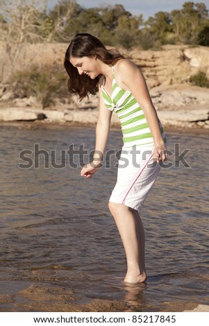 A woman walking in to the water with her feet with a smile on her face.