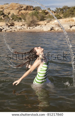 A woman standing waist deep in the water flipping her hair to make a water rainbow.