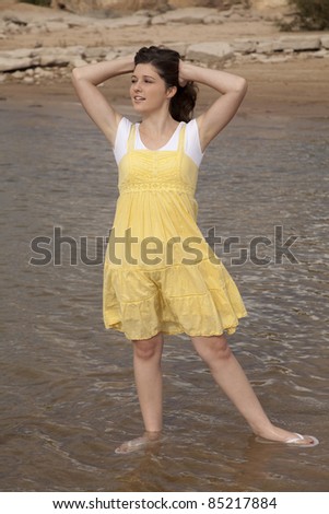 A woman standing in the water in her yellow dress with her hands in her hair.