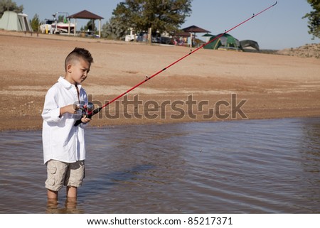 a young boy standing out in the water fishing with his fishing pole.
