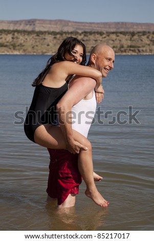 a man giving his woman a ride on his back out into the water with smiles on their faces.