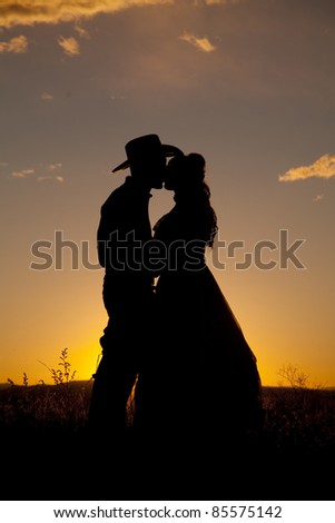 A cowboy is kissing a woman in the sunset.
