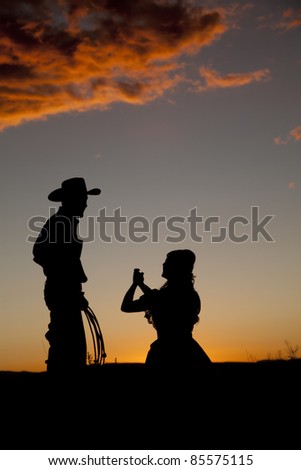 A woman is on her knees pleading with her cowboy in the sunset.