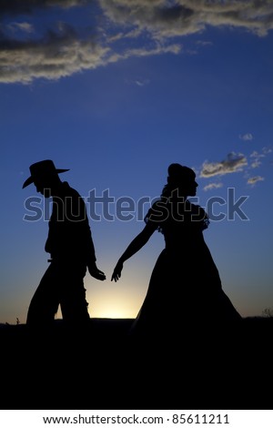 A cowboy and a woman are silhouetted in the sunset as they walk away from each other.