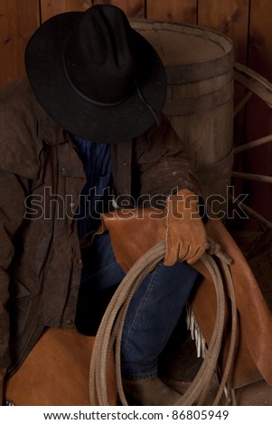 a cowboy kneeling down by a wine barrel looking down.