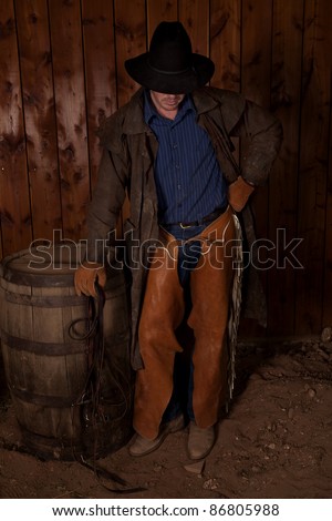 A cowboy standing up in the dirt with his head down.