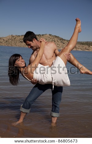 A man holding his girl up in the air dipping her while he stands in the water.