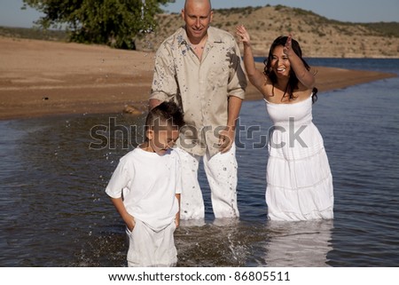 A family playing in the water with their clothes on the mom is splashing her son with water.