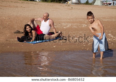 Parents sitting on the beach watching their son play in the water.