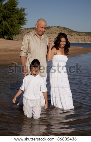 A family standing and playing in the water with their clothes on with smiles on their faces.