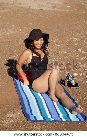 A woman sitting on the beach on her towel relaxing and taking it easy.