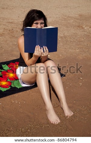 A woman sitting on her beach towel peeking over the top of her book.
