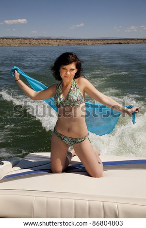 A woman kneeling on the back of the boat enjoying the breeze playing with her sarong.