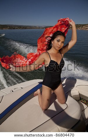 a woman kneeling on the back of a boat letting the wind blow her sarong in the wind.
