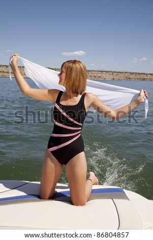 A woman kneeling on the back of a boat holding out her white sarong in the breeze.