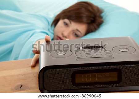 A woman reaching out for her alarm clock trying to get a few more minutes of sleep in.