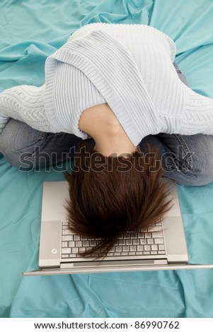 A woman in her bed with her head laying on top of her computer keyboard asleep.