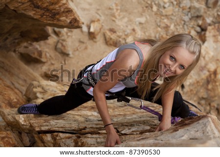 A woman looking up at the camera while she is rock climbing.