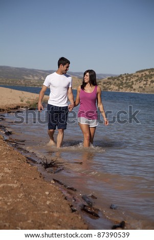 A couple walking in the water and holding hands looking in to each others eyes.