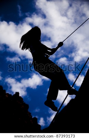 A silhouette of a woman rock climbing with ropes.
