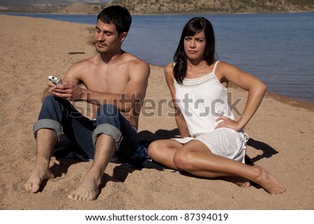 A woman is mad that her man is texting on his phone while they are at the beach.