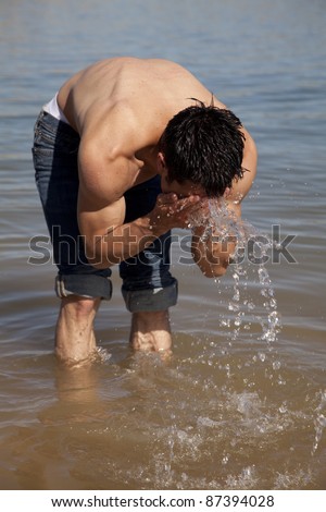 A man leaning over in the lake to splash water on his face to cool him off.