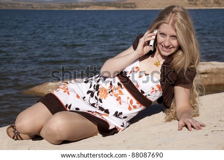 A woman laying in the outdoors by the ocean talking and smiling on the phone.