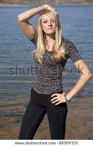A woman standing by the lake enjoying the sun with a small smile on her face.