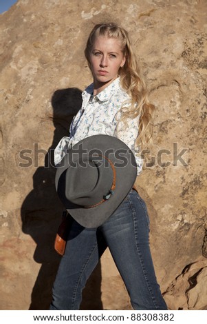 a woman holding on to her cowgirl hat with a serious expression on her face.