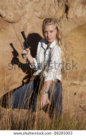 A woman kneeling down in the grass holding on to a gun with  a serious expression on her face.