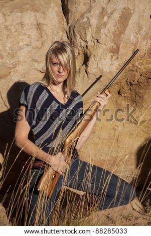 A woman kneeling down in the grass holding a rifle.