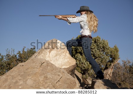 a woman standing in her western wear in the outdoors holding a gun.