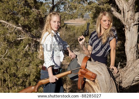 Two women standing together holding their weapons in their western outfits.