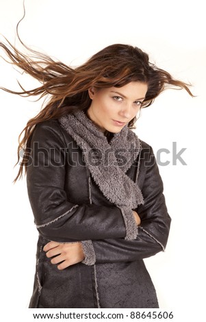A woman wrapped up in her gray coat with a serious expression on her face with  the wind blowing her hair.
