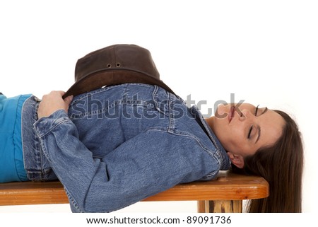 A woman laying on a bench asleep with her cowgirl hat laying on her chest.