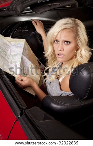 A woman sitting in her car and looking at a road map with a confused expression on her face.