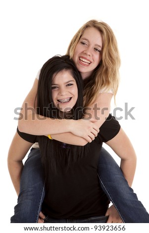 A teen girl giving her friend a piggy back ride laughing.