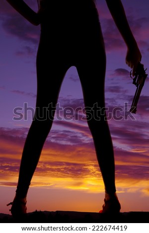 A silhouette oh a womans legs, with her hand  holding on to a pistol.