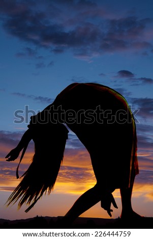 A silhouette of a woman in her dance clothes doing a back bend in the outdoors.