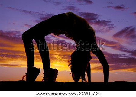A silhouette of a woman doing a back bend in the outdoors.