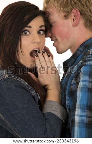 a man whispering into his woman\'s ear she has a shocked expression on her face.
