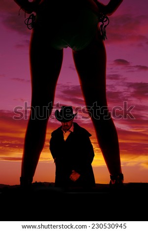 a silhouette of a woman\'s legs with her hand on her hip with her cowboy in the middle of them.