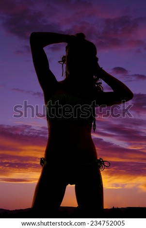 A silhouette of a woman kneeling with her hands in her hair.