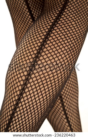 A womans legs in black fishnet stockings up close from the back crossed.
